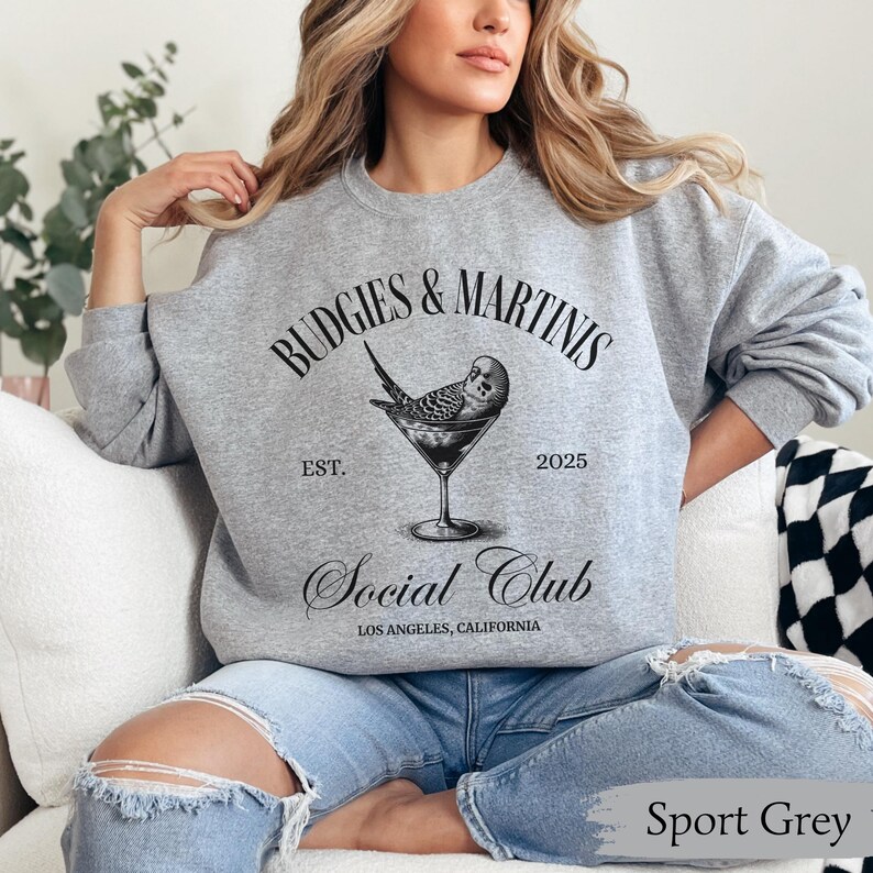 May include: A gray sweatshirt with the text "Budgies & Martinis Social Club Est. 2025 Los Angeles, California" and a black and white illustration of a budgie in a martini glass.