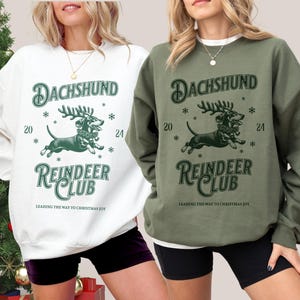 May include: Two white and green sweatshirts with a dachshund wearing reindeer antlers and the text "Dachshund Reindeer Club" and "Leading the way to Christmas joy".
