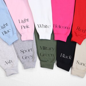 May include: A variety of sweatpants in different colors, including light blue, light pink, white, red, black, sand, ash, sport grey, and military green. The sweatpants are laid out on a white surface.