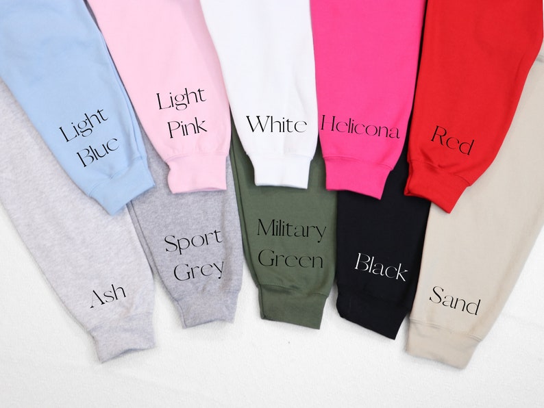 May include: A variety of sweatpants in different colors, including light blue, light pink, white, red, black, sand, ash, sport grey, and military green. The sweatpants are laid out on a white surface.