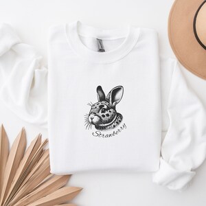 May include: White sweatshirt with a black and white illustration of a rabbit with the text "Strawberry" underneath.