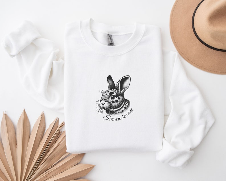 May include: White sweatshirt with a black and white illustration of a rabbit with the text "Strawberry" underneath.