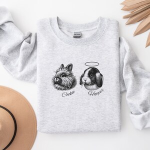 May include: A gray sweatshirt with a black and white illustration of two bunnies. The bunny on the left is named "Cookie" and the bunny on the right is named "Hopper".