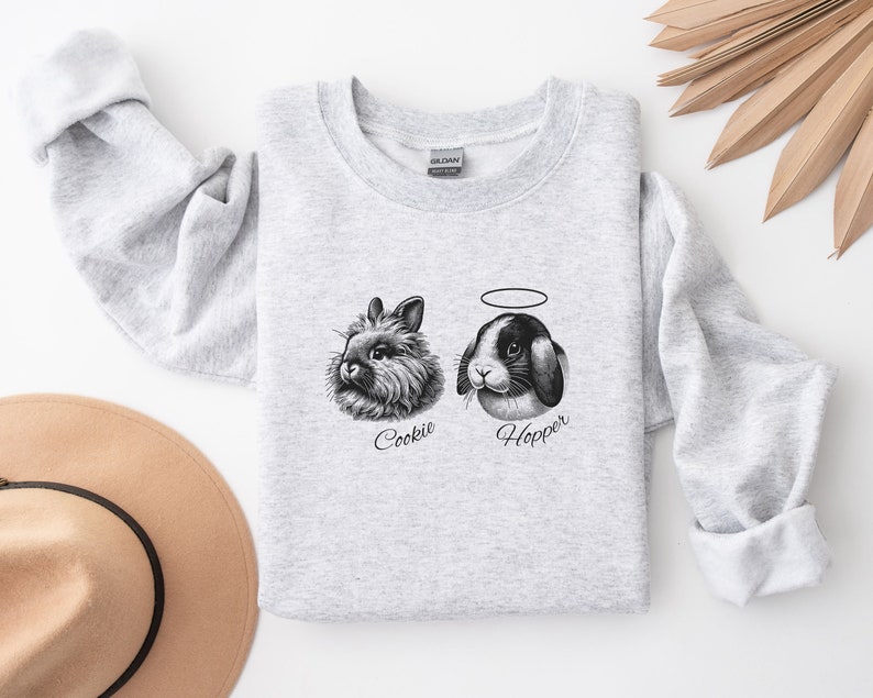 May include: A gray sweatshirt with a black and white illustration of two bunnies. The bunny on the left is named "Cookie" and the bunny on the right is named "Hopper".