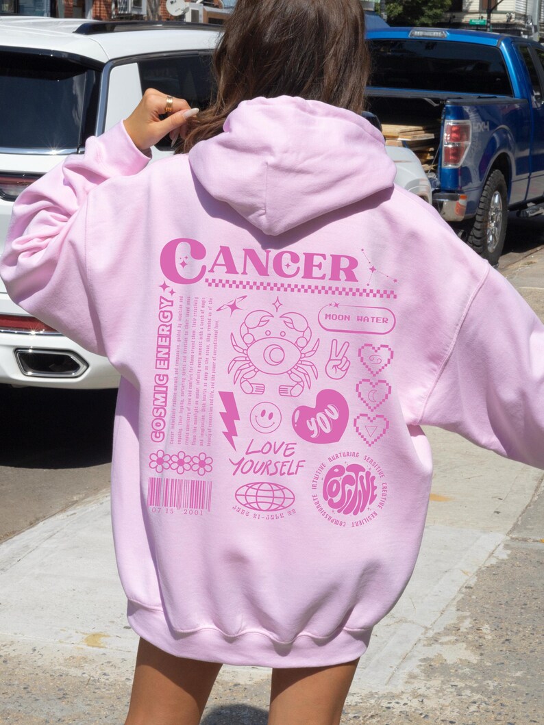 May include: Pink hoodie with a graphic design featuring the zodiac sign Cancer, the text "Cancer", "Moon Water", "Cosmic Energy", "Love Yourself", "You", and "Positive".
