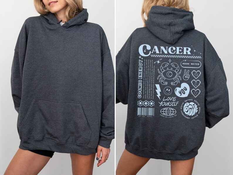 May include: A dark gray hooded sweatshirt with a white graphic on the back that says "Cancer" and includes a crab, stars, hearts, and the text "Cosmic Energy", "Love Yourself", and "You".