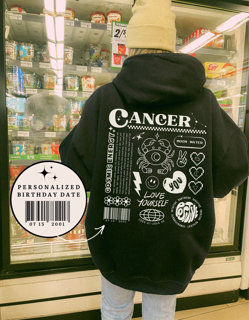May include: Black hoodie with a white graphic print of the zodiac sign Cancer. The graphic includes the words "Cosmic Energy", "Moon Water", "Love Yourself", and "Positive". The hoodie also has a personalized birthday date barcode.