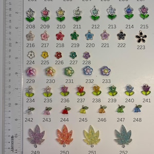 May include: A collection of assorted small charms arranged in rows, labelled 201 through 252, featuring various flower, tulip, and leaf shapes in multiple colours. A Westcott ruler is positioned on the left side, showing measurements in inches.