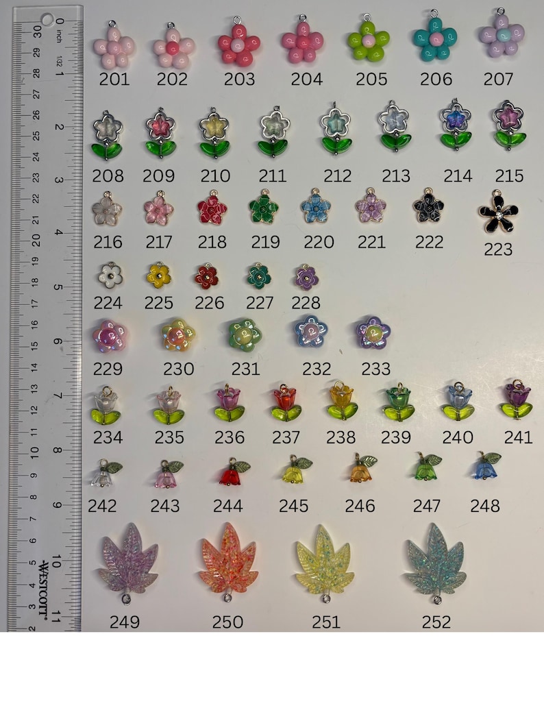 May include: A collection of assorted small charms arranged in rows, labelled 201 through 252, featuring various flower, tulip, and leaf shapes in multiple colours. A Westcott ruler is positioned on the left side, showing measurements in inches.