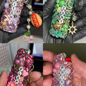 May include: Four lighters decorated with colourful rhinestones, beads, and charms. The lighters feature letter beads spelling BITCH, CUNT, FLOOP, and PRINCESS. Each lighter includes dangling charms like a hot dog, sun, rainbow, and cherries.