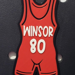 May include: Red wrestling singlet with black trim and white lettering. The singlet has the name "Winsor" and the number "80" on the front.