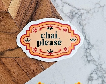 May include: A sticker with the text "chai, please" in dark green, set against a peach background with floral accents. The sticker has a decorative border in orange and red. The background is a mix of wood and marble.