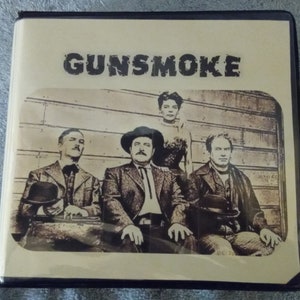 May include: A vintage DVD case with a sepia-toned image of four people. The case has the title "GUNSMOKE" printed in bold, white letters on a tan background.