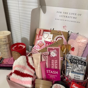 Puede incluir: Una caja de regalo rosa llena de artículos de temática romántica. Incluye una vela, calcetines, lociones, té, una piruleta y una caja de caramelos Sweethearts. La caja está etiquetada como "For the Love of Literature" y "Blind Date with a Book Box".