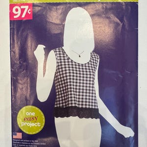 Puede incluir: Un sobre de patrón de costura Simplicity Sew Simple A8122 para tallas XS-XL. El frente presenta un gráfico de una blusa sin mangas con un patrón de cuadros vichy en blanco y negro y un dobladillo de encaje negro. Incluye "one easy project".