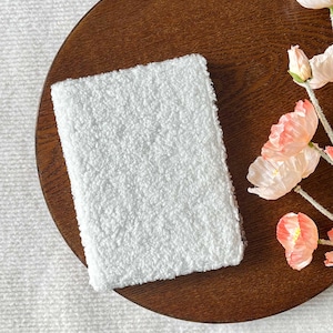 Pode incluir: Um caderno branco e felpudo em uma bandeja de madeira marrom com flores cor-de-rosa.