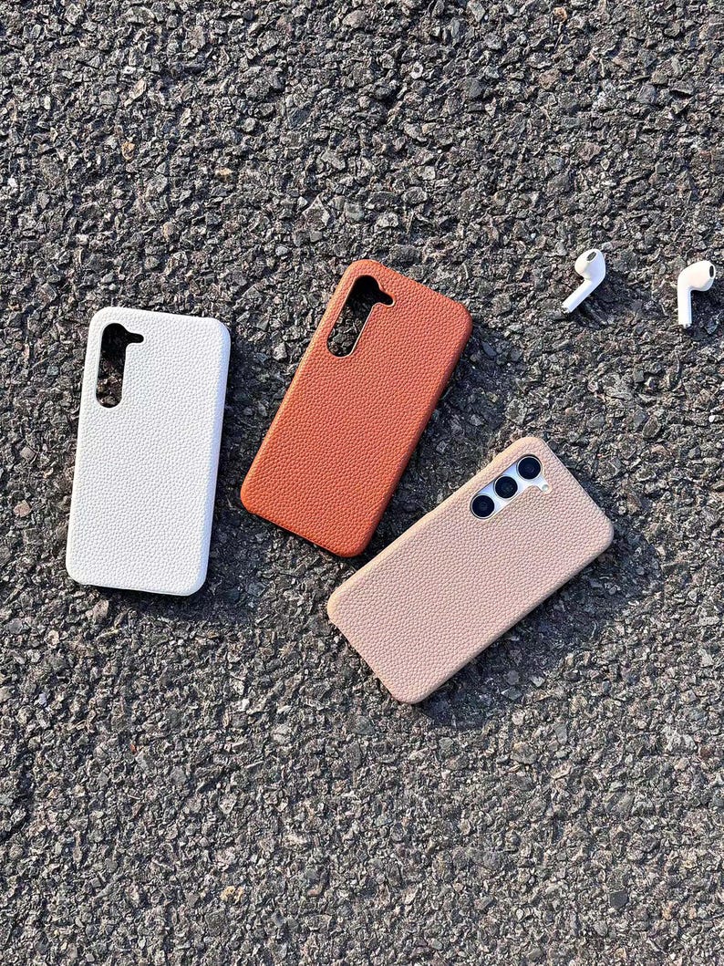 Puede incluir: Tres fundas para tel&eacute;fono de diferentes colores: blanco, marr&oacute;n y beige. Las fundas est&aacute;n hechas de un material texturizado y tienen un recorte para el objetivo de la c&aacute;mara.