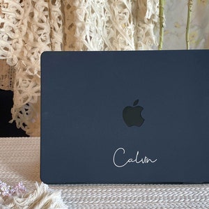 May include: A dark blue laptop with a silver Apple logo and the name "Calvin" written in white cursive on the lid.