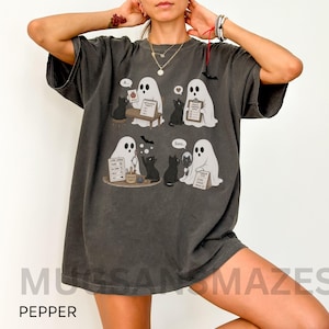 May include: A charcoal gray short-sleeve t-shirt featuring a graphic print of four scenes with white ghosts and black cats. The illustrations include speech bubbles and text labels like Apple, Articulation Targets, Core Words, and Ssss.