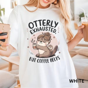 May include: White t-shirt with a graphic of an otter holding a cup of coffee and the text "Otterly Exhausted, But Coffee Helps".