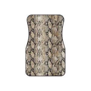 May include: A car floor mat with a snakeskin design. The mat displays a repeating pattern of tan, brown, and black scales, mimicking reptile skin. It has a black border and a curved shape, suitable for a car's footwell.