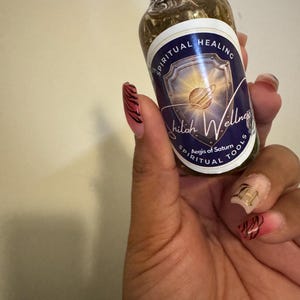 May include: A small glass bottle with a black cap, filled with a golden liquid. The label reads "Spiritual Healing" and "Shiloh Wellness Spiritual Tools." The bottle is held in a hand with painted nails.
