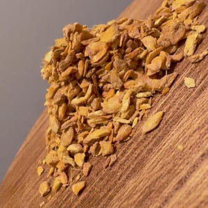 May include: A pile of dried, sliced ginger pieces, with a warm, golden-brown color. The ginger is arranged on a wooden surface, showcasing the texture and shape of the dried spice. The image highlights the natural, organic quality of the ginger.