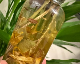 May include: A clear glass bottle filled with a golden liquid and containing dried plant material. The bottle has a black screw-on cap.