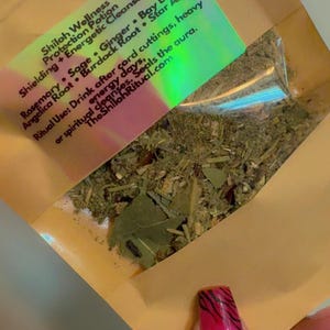 May include: A clear plastic bag filled with dried herbs and leaves. A label on the bag lists ingredients like rosemary, sage, and ginger. The text on the label reads "Shiloh Wellness Protection Potion".