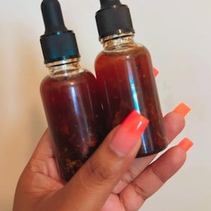 May include: Two small glass bottles with black dropper tops filled with a dark brown liquid. The bottles are held in a hand with bright orange nail polish.