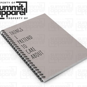 May include: A grey spiral-bound notebook with the text "THINGS I PRETEND TO CARE ABOUT" in black. The notebook is from Summit Apparel.