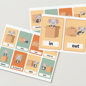 May include: Flashcards for education showing a cartoon mouse and a cardboard box. The cards illustrate prepositions such as "in," "out," and "above." The cards have a white border and are set against a light background.