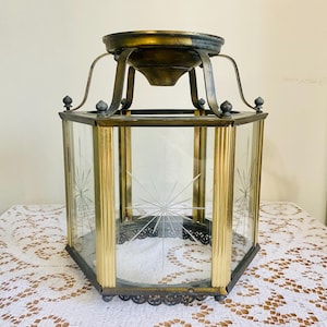 May include: Vintage brass and glass lantern with a starburst design etched into the glass panels. The lantern has a hexagonal shape with decorative metal accents and a detailed top and bottom. A classic lighting fixture.
