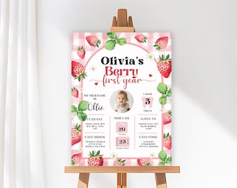 May include: A pink and white gingham-patterned sign with the text "Olivia's Berry first year" and a photo of a baby. The sign includes information about the baby's nickname, favorite songs, and favorite foods. The sign is 23 inches tall and weighs 20 pounds.