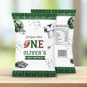 Könnte beinhalten: Zwei weiße Chipstüten mit Football-Motiv. Die Tüten zeigen einen grünen Footballhelm, einen Football und ein Trikot. Der Text enthält "first year down ONE OLIVER'S FIRST BIRTHDAY" und "Nutrition Facts".