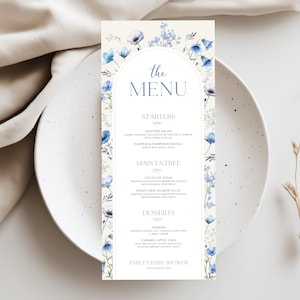 May include: A menu card with a floral design, featuring blue flowers and greenery. The text "the MENU" is at the top, with sections for starters, main entree, and desserts. The event is a baby shower.
