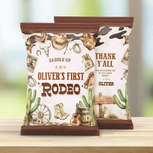 Op de afbeelding: Twee bruin-witte traktatiezakjes met een western thema. De zakjes bevatten illustraties van cowboylaarzen, een gitaar en cactussen. De tekst op de zakjes luidt "Oliver's First Rodeo" en "Thank Y'all".