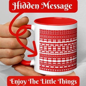Peut inclure: Mug en céramique blanche avec intérieur, anse et motif décoratif rouges. Le mug porte les inscriptions "Hidden Message" et "Enjoy The Little Things" en rouge.