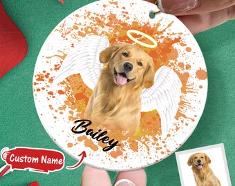 May include: A white round ornament with a watercolor-style image of a golden retriever with angel wings. The dog is looking at the viewer and has a halo above its head. The text "Bailey" is written below the dog.