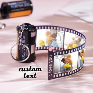 May include: A black film camera keychain with a silver key ring and a film strip with photos. The film strip has the text "I love you" and a pink heart. The camera has the text "PORTRA 200" and "Professional Film" on it. The text "custom text" is below the camera.