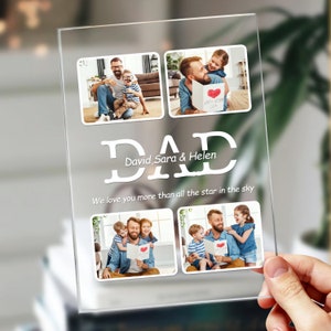 May include: A clear acrylic photo frame with four pictures of a father and his children. The frame has the word "DAD" in large white letters with the names "David, Sara & Helen" written below. The text "We love you more than all the star in the sky" is written below the names.