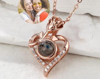 May include: Rose gold necklace with a heart-shaped pendant featuring a small round projection screen and a rose design. The pendant is adorned with clear cubic zirconia stones.