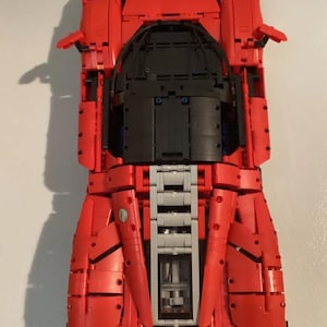 May include: A red Lego Ferrari F40 model car with black and gray details. The car is built from Lego bricks and is a replica of the real Ferrari F40.