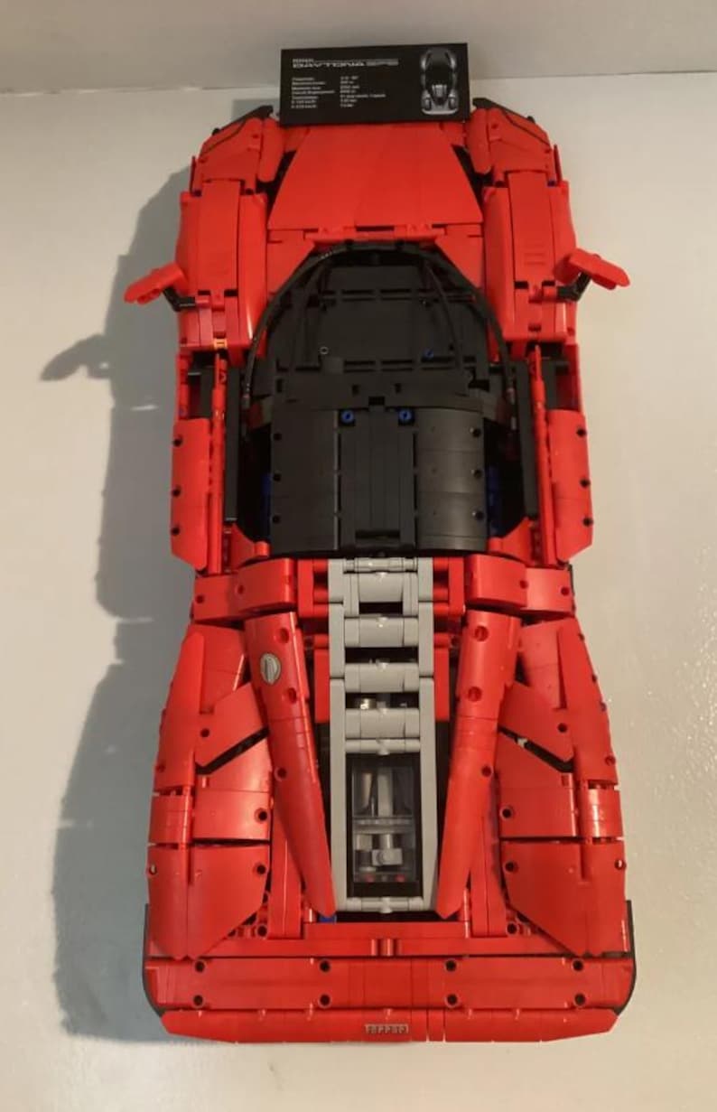 May include: A red Lego Ferrari F40 model car with black and gray details. The car is built from Lego bricks and is a replica of the real Ferrari F40.