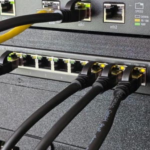 以下が含まれることがあります： ラックに取り付けられた黒いTP-Link TL-SG608E 8ポートギガビットイージースマートスイッチ。デバイスには複数のイーサネットポートがあり、黒いケーブルが接続され、ネットワーク接続を示すアクティブな黄色のLEDステータスライトが表示されています。