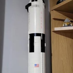 May include: A white and black Lego model of the Saturn V rocket with the words "USA" printed on the side. The rocket is mounted on a black stand.