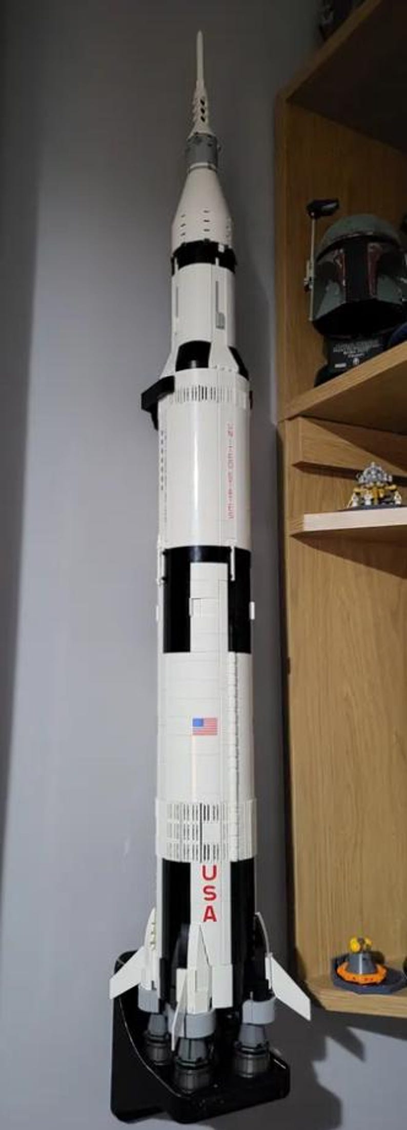 May include: A white and black Lego model of the Saturn V rocket with the words "USA" printed on the side. The rocket is mounted on a black stand.