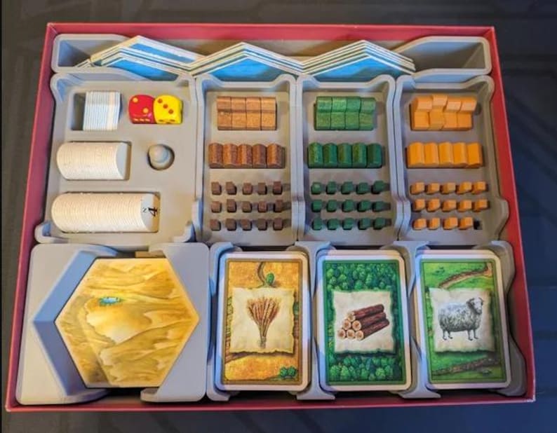 May include: A board game organizer with various game pieces. Includes dice, wooden blocks, cards with illustrations of wheat, logs, and a sheep. The organizer is divided into compartments with a red border.