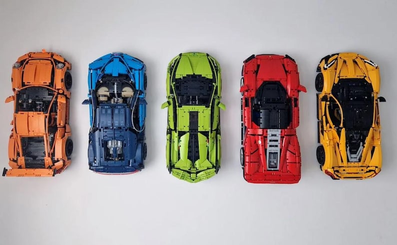 May include: Five toy cars in different colors: orange, blue, green, red, and yellow. The cars are all facing forward and have a similar design.