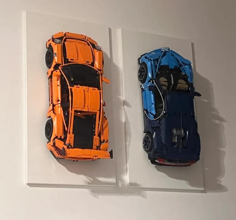 May include: Two Lego car models mounted on white canvases. The car on the left is orange and the car on the right is blue.